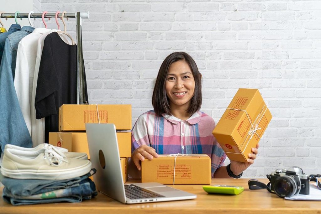 Businesswoman with sealed boxes and laptop on a wooden desk packaging custom clothing items
