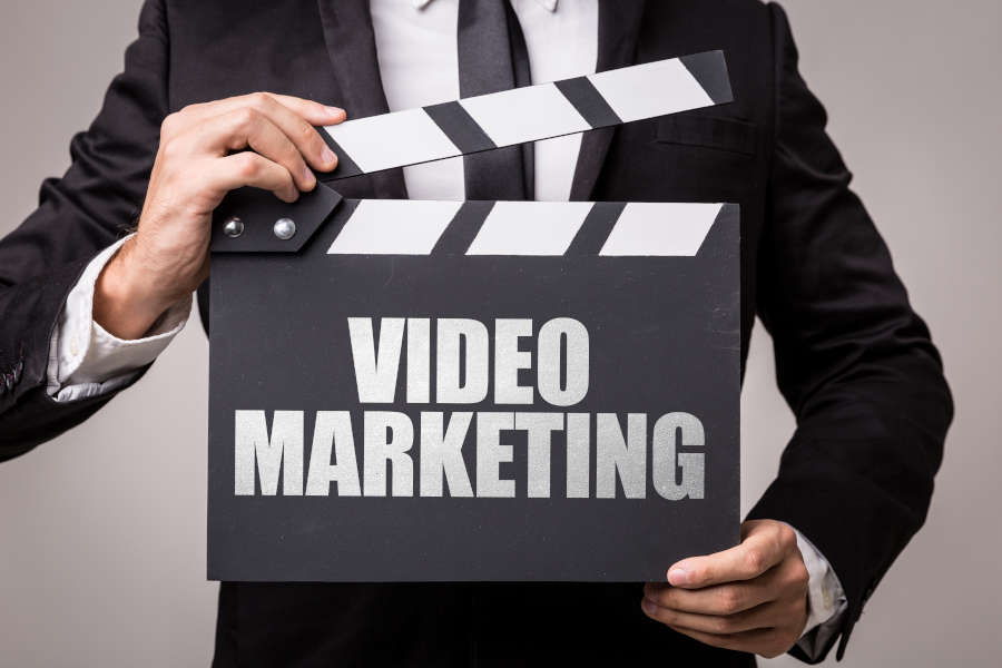 Person in a black suit and white shirt holding a film clapperboard that says video marketing